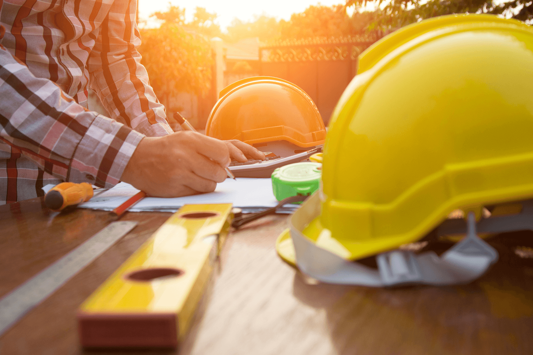 Bauunterlagen und gelber Schutzhelm auf Holztisch bei Sonnenlicht, Symbol für Planungssicherheit und solide Bauausführung bei Vionda Haus.
