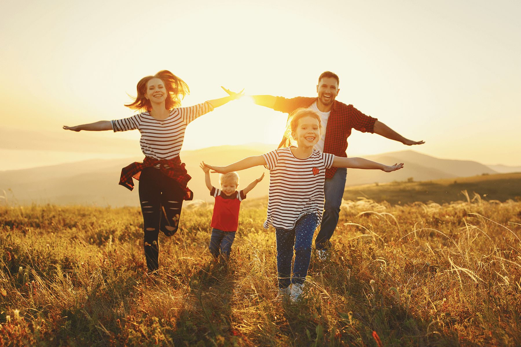 Familie mit zwei Kindern läuft Hand in Hand durch ein Feld im Sonnenlicht, steht für Freiheit und Lebensfreude