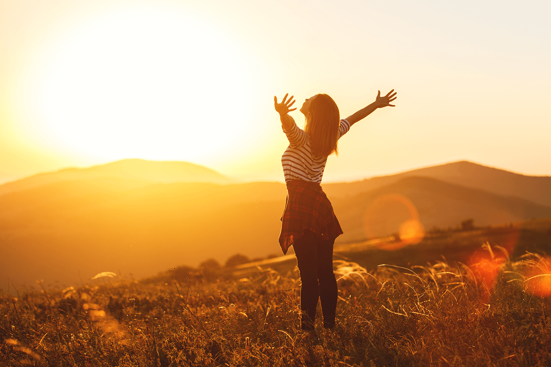 Frau steht mit ausgebreiteten Armen im Sonnenuntergang und symbolisiert Freiheit und Lebensfreude