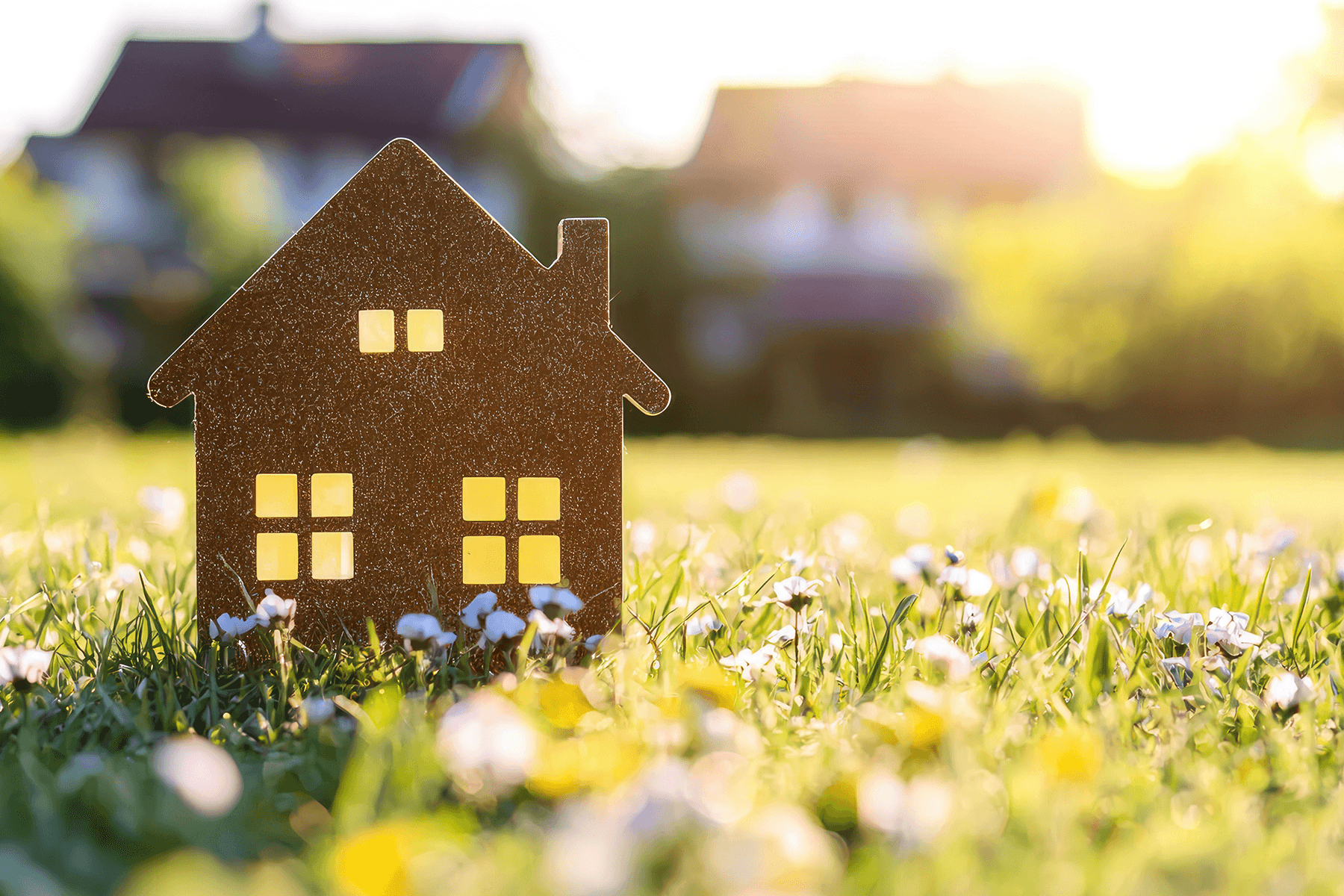 Kleine Holzhausfigur steht auf einer Wiese im Sonnenlicht, Sinnbild für Nachhaltigkeit und Eigenheimträume