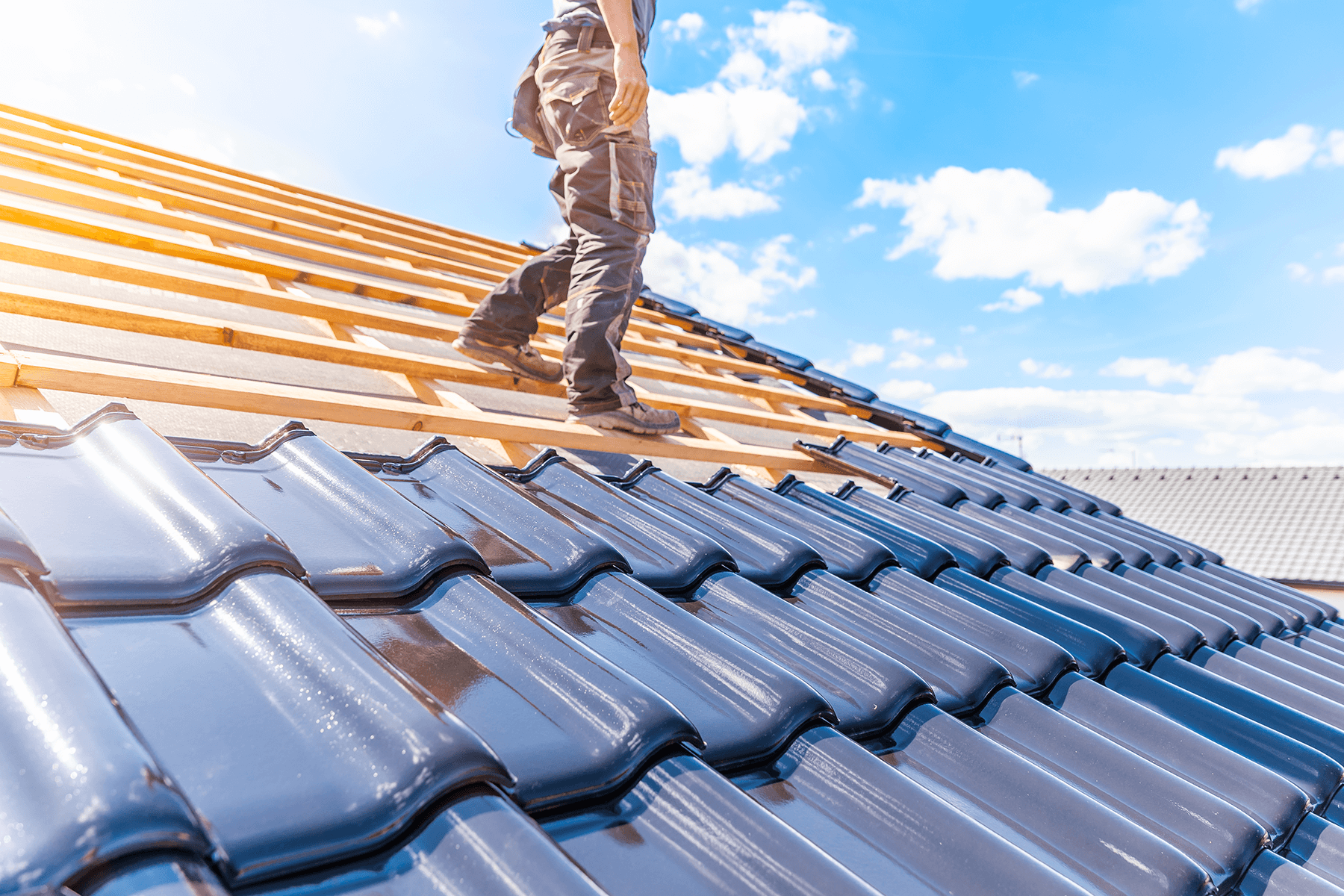 Handwerker arbeitet auf dem Dach eines im Bau befindlichen Bungalows mit dunklen Dachziegeln. Sinnbild für hochwertige Verarbeitung und langlebige Bauqualität bei Vionda.