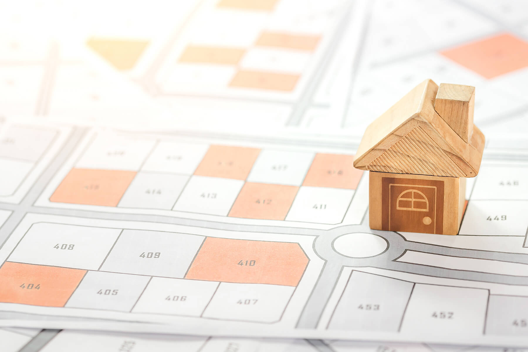 Haus Modell auf einem Grundstücks- und Bebauungsplan, symbolisch für Grundstücksauswahl und Planung.