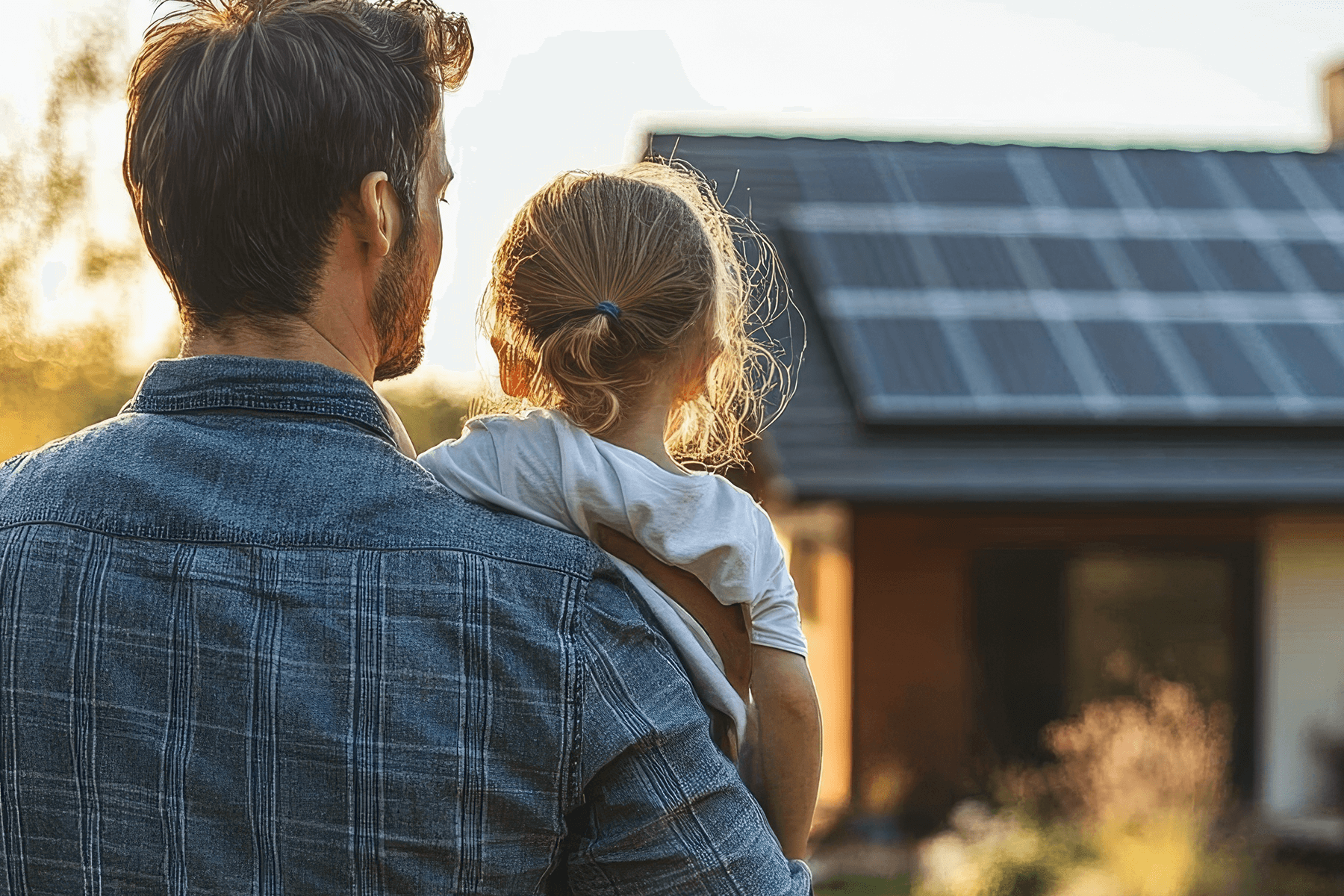 Vater hält Tochter im Arm vor einem modernen Bungalow mit Solaranlage – Symbol für nachhaltiges und zukunftssicheres Bauen mit Vionda.