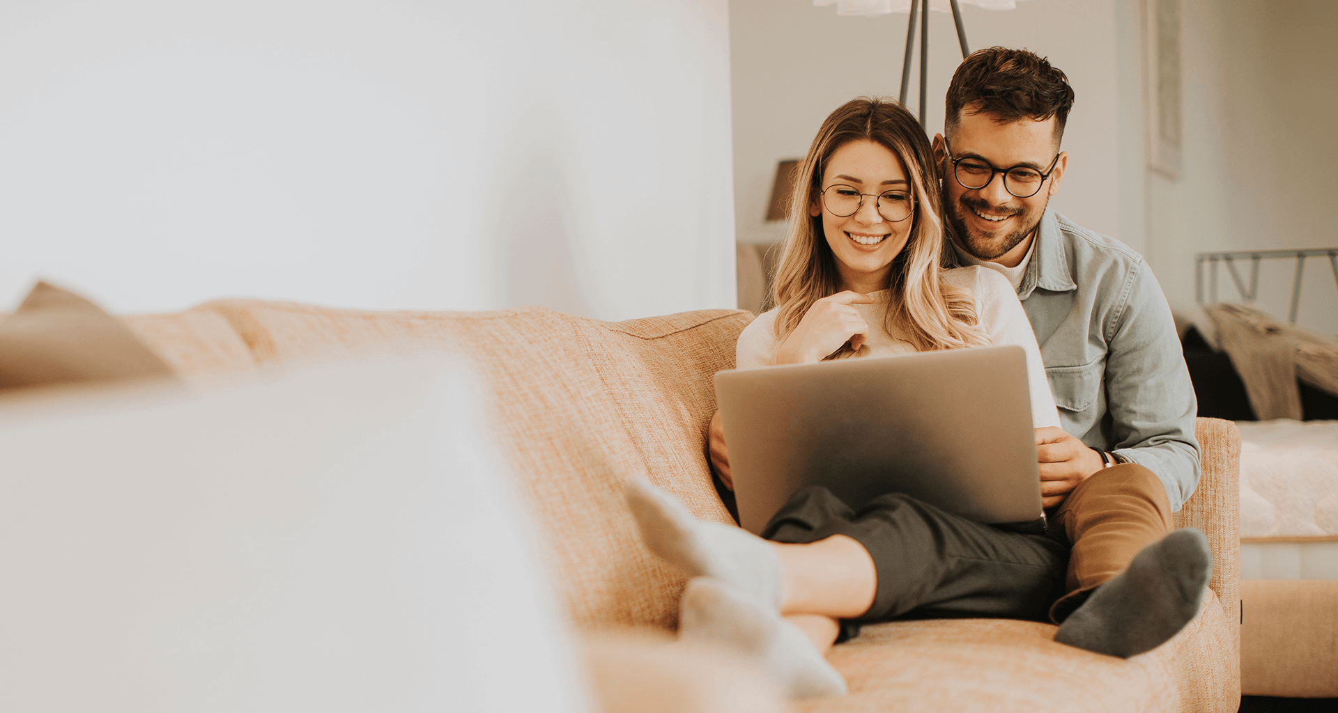 Paar sitz eng umschlungen auf dem Sofa und recherchiert im Internet über eine Investition eines Bungalows.