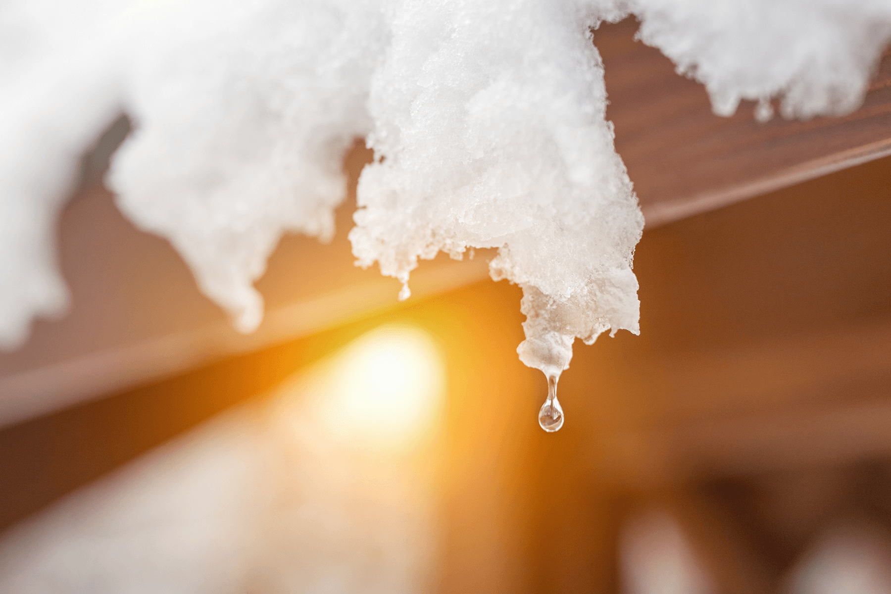 Schnee schmilzt am Dachrand eines Hauses und tropft ab – Detailaufnahme zur Veranschaulichung von Dachneigung und Wasserabführung im Winter.