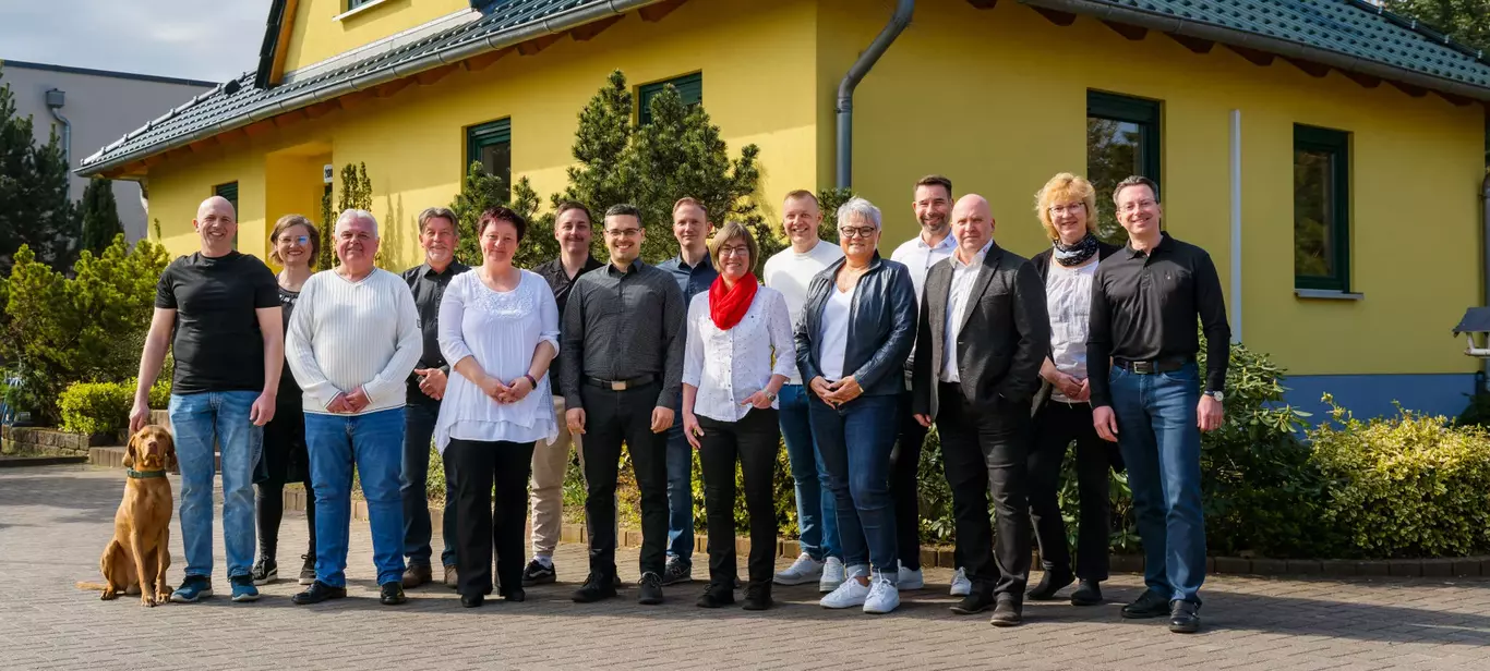 Zahlreiche Menschen vor einem massiven Bungalow zeigen stellen sich als Team von Vionda Haus vor.