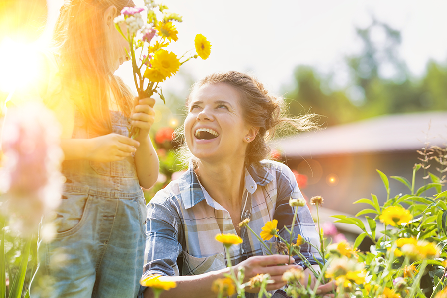 Mutter und Kind pflücken gemeinsam Blumen im Garten und lachen dabei.