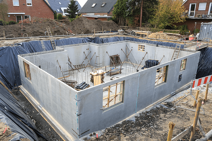 Rohbau eines Kellers mit Betonwänden und Bewehrung auf einer Baustelle in einem Wohngebiet.