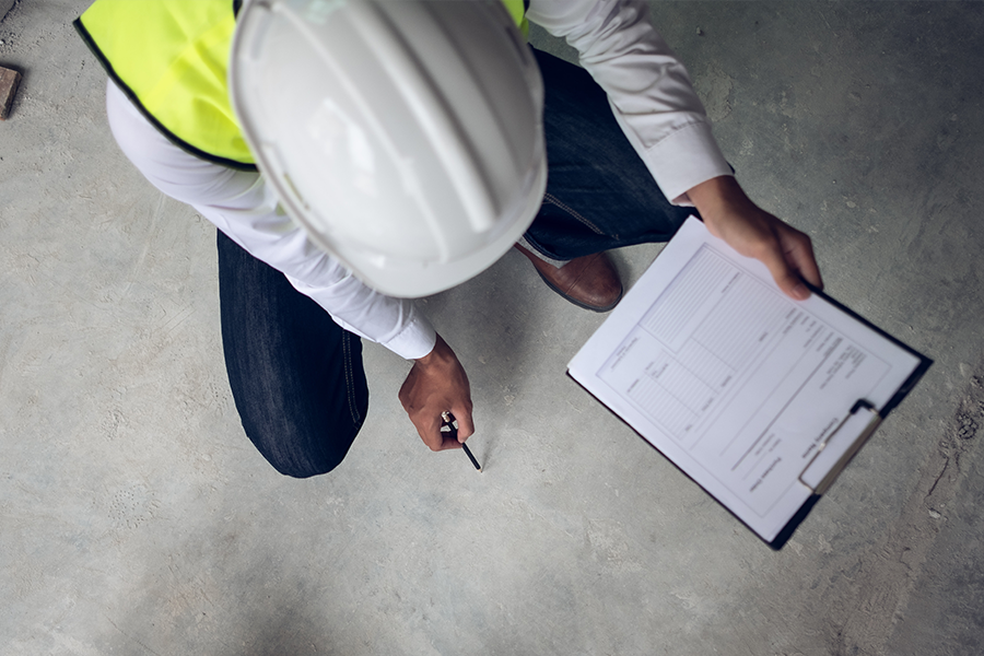 Bauarbeiter prüft Qualität der Betonplatte und hält dabei eine Checkliste in der Hand und in der anderen einen Stift