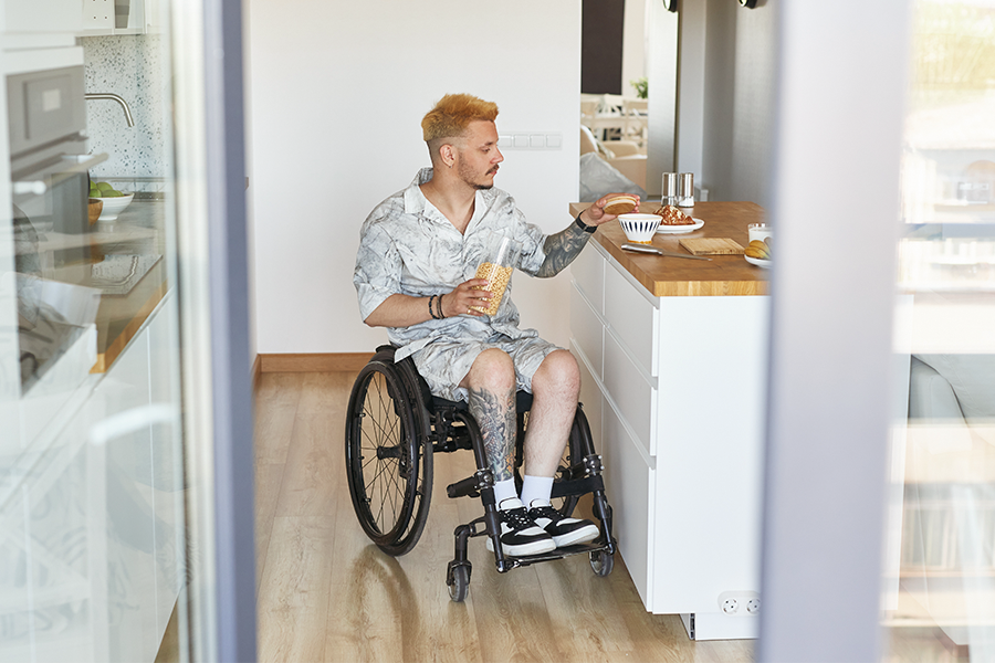 Mann im Rollstuhl bewegt sich selbstständig in einer barrierefrei gestalteten Küche und greift nach Lebensmitteln auf einer Arbeitsfläche